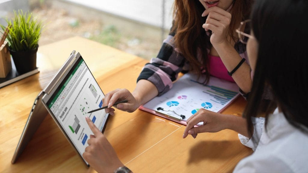 Two women pointing at a Lenovo Yoga 9i on table Two women pointing at a Lenovo Yoga 9i on table