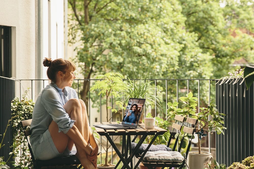 Woman sitting at a table in an outdoor patio engaged in a video call with laptop on table