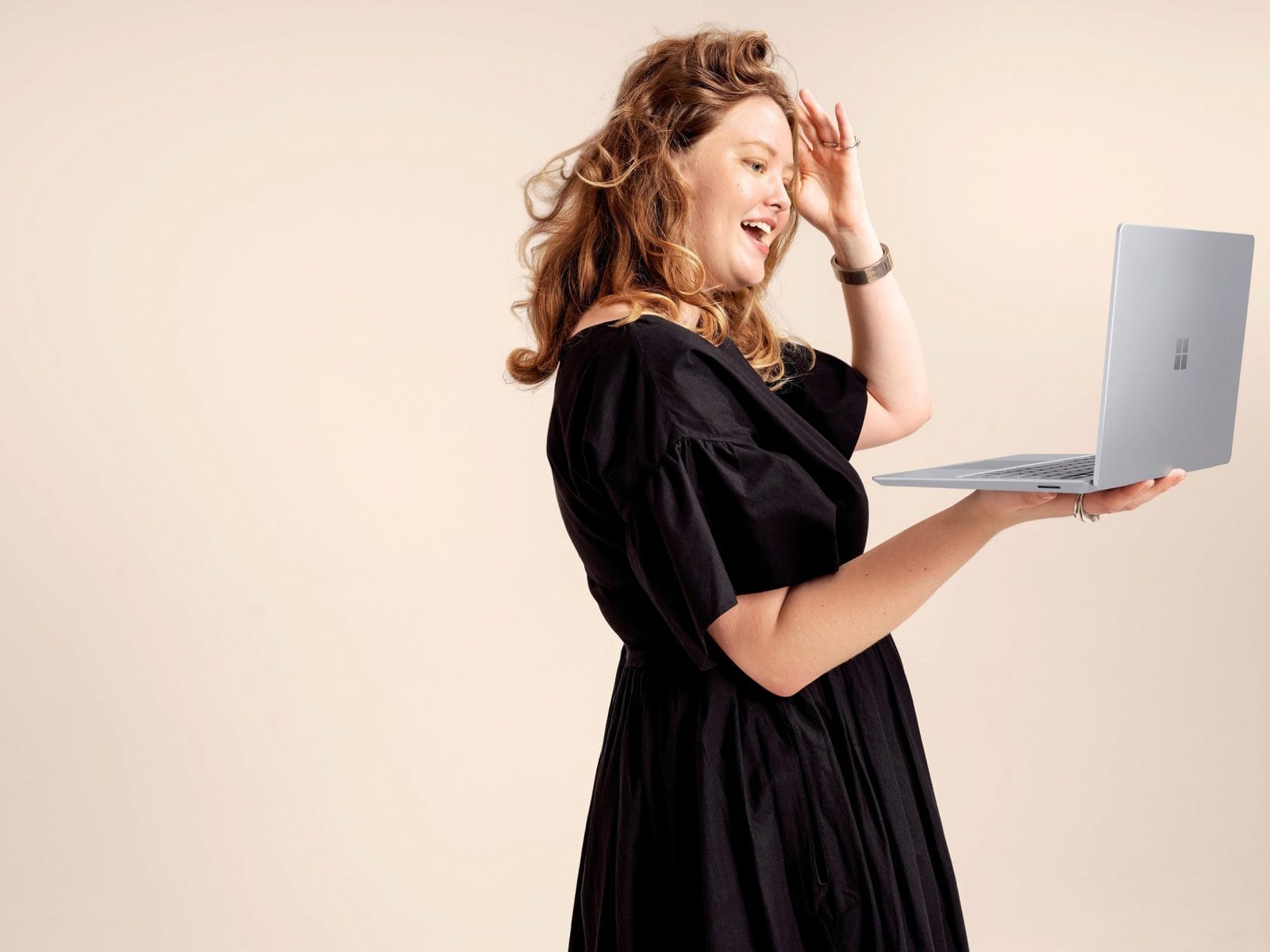 person in a black dress holds a laptop device in one hand